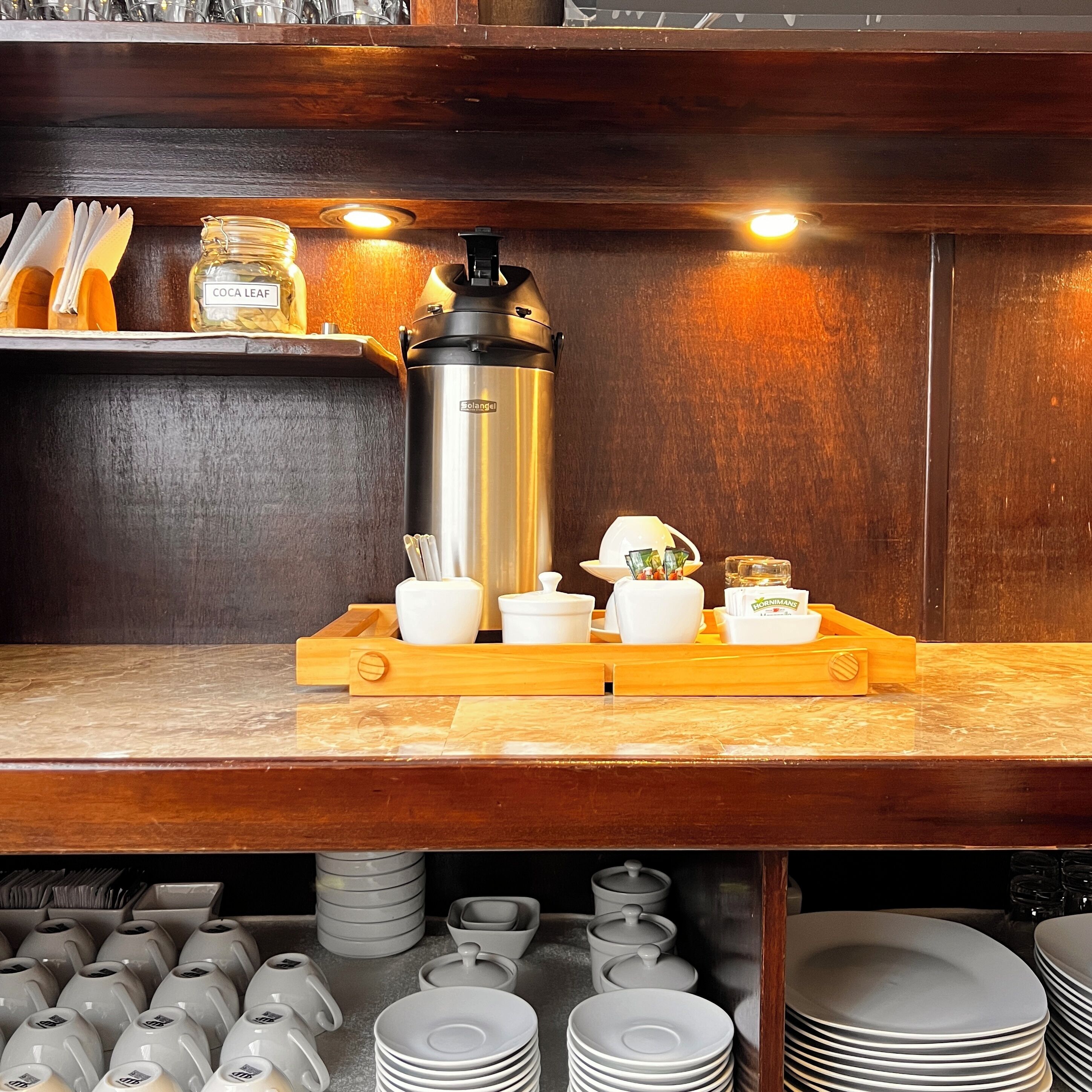 A coffee station with a coffee maker, cups, and condiments.