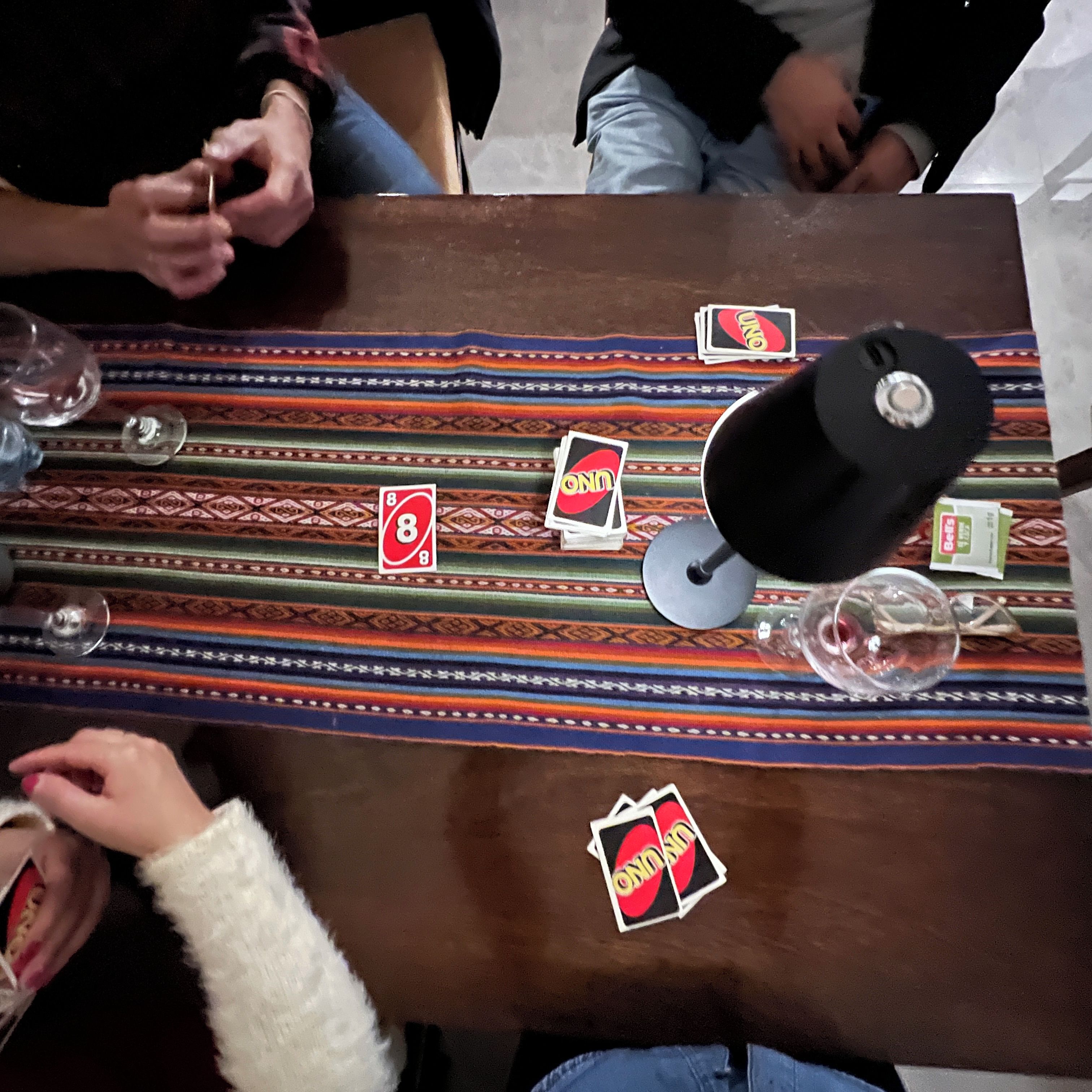 A table with a patterned tablecloth, playing cards, and a black object on it.