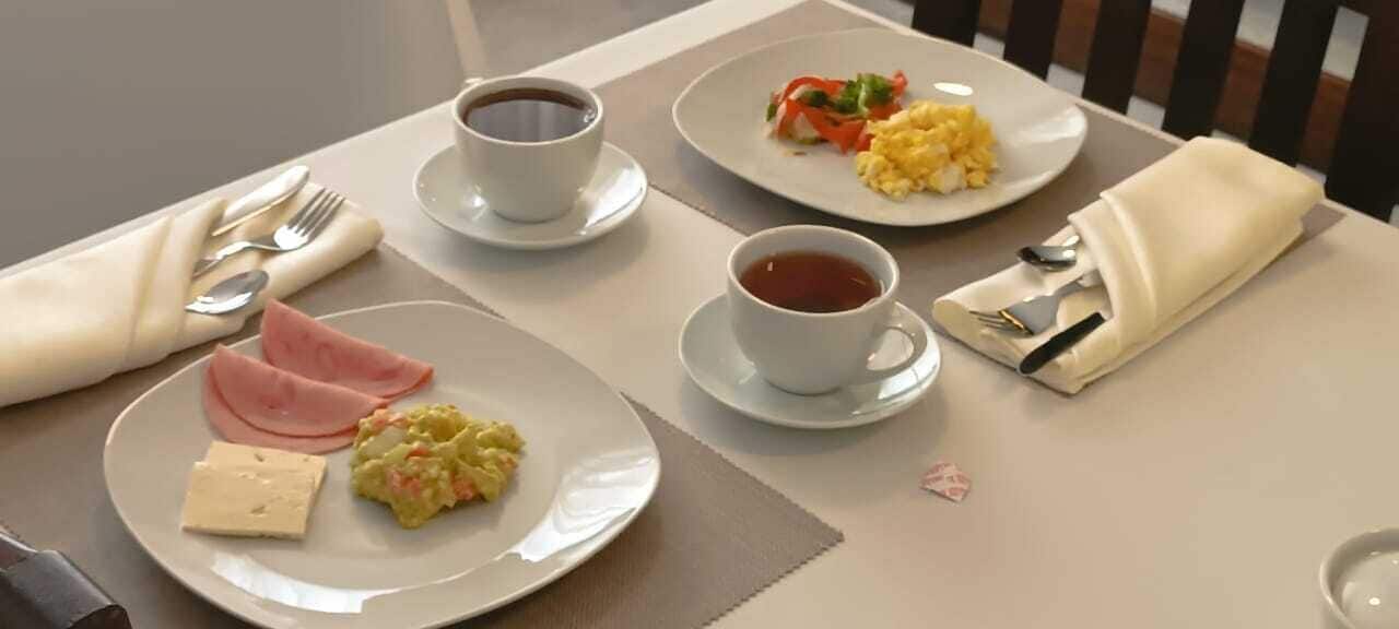A breakfast setting with plates of food, cups of coffee, and a napkin with utensils.