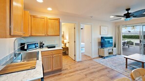 A modern kitchen with wooden cabinets, a stainless steel sink, and a microwave. There is a dining area with a table and chairs, and a ceiling fan.