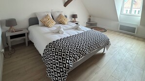 Un dormitorio con una cama grande, dos mesitas de noche, una planta colgante y un ventanal con vistas a edificios.