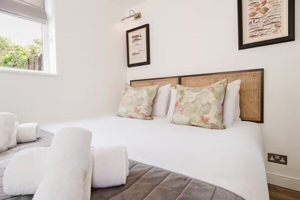 A neatly made bed with floral pillows, a headboard with a woven pattern, and a framed picture on the wall. - Cosy Studio Annexe Central Cheltenham (Cheltenham)