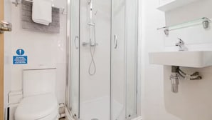 Un baño moderno con ducha envuelta en vidrio, inodoro blanco y repisa de vidrio sobre el lavamanos.