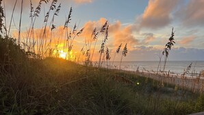 A coastal landscape with a sunset, grassy dunes, and a wooden boardwalk. - 4BR Hatteras Retreat • 5-Min Walk to Beach • Pet Friendly (Hatteras)