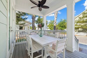 Une véranda abritée avec une table et des chaises, un ventilateur de plafond et une vue sur les palmiers et les maisons.