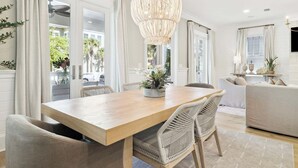 A dining area with a wooden table, wicker chairs, a hanging light fixture, and a view through a glass door.