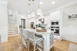 Une cuisine avec des meubles blancs, un îlot central et des luminaires suspendus.