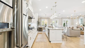A modern kitchen with stainless steel appliances, a central island, pendant lighting, and a view of the dining area.