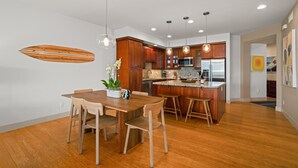 A modern kitchen with wooden cabinets, a granite countertop, and stainless steel appliances. There is a dining area with a wooden table and chairs.