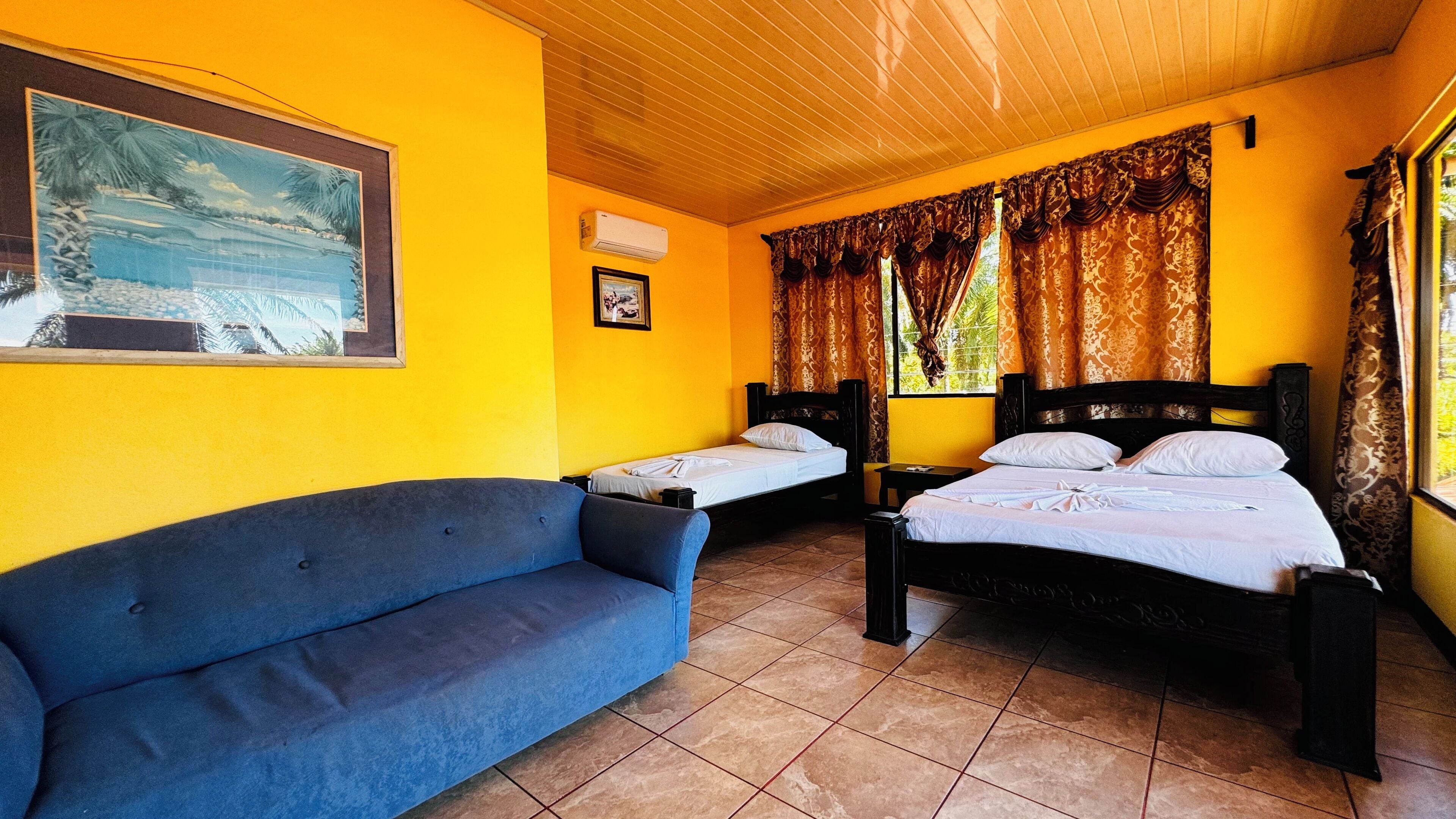 A room with two beds, a blue sofa, and a painting on the wall.