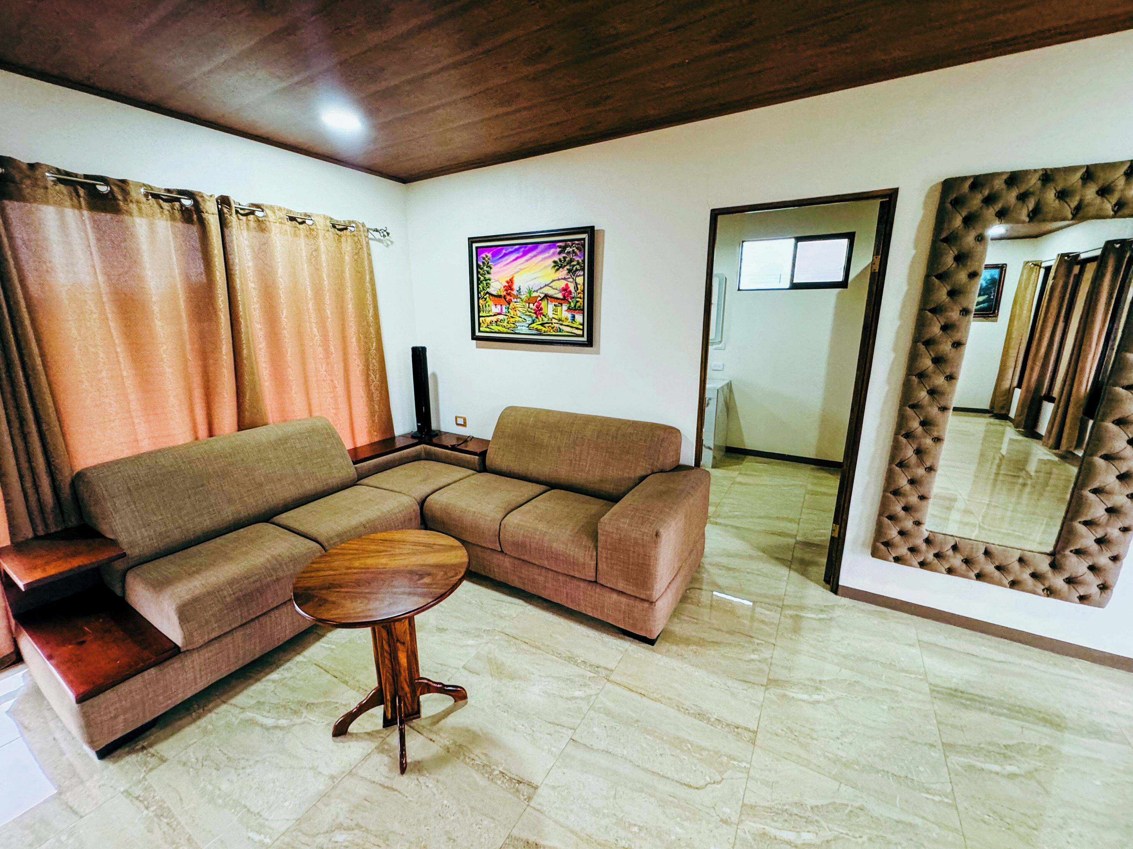 A living room with a sectional sofa, a round wooden coffee table, a large mirror, and a painting on the wall.