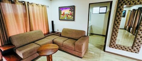 A living room with a sectional sofa, a round wooden coffee table, a large mirror, and a painting on the wall.