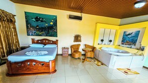 A hotel room with a bed, a small table, two armchairs, a sofa, a bathtub, and a large window. - Los Angeles Hotel & Resort  (Parrita)