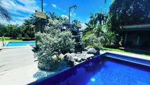 A swimming pool with a stone and plant border, surrounded by a clear sky and lush greenery. - Los Angeles Hotel & Resort  (Parrita)