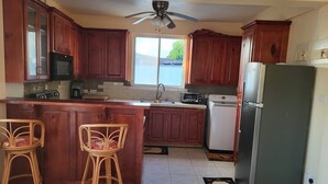 A kitchen with wooden cabinets, a central island with two bar stools, a ceiling fan, and a refrigerator. - 3-bedroom house in the Nature Isle, Canefield, Dominica (Canefield)