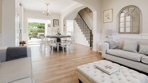 A spacious living room with a high ceiling, a dining area with a round table, and a staircase leading to an upper floor. - Stylish Townhouse Annexe Cheltenham (Cheltenham)