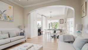 A spacious living room with a white sofa, a tufted ottoman, and a dining area with a white table and chairs. - Stylish Townhouse Annexe Cheltenham (Cheltenham)
