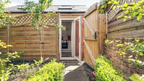 A wooden shed with a door leading to a brick interior, surrounded by greenery and a stone pathway. - Stylish Townhouse Annexe Cheltenham (Cheltenham)