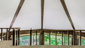 A high-ceilinged room with a wooden beam structure and a balcony with a view of greenery.