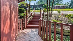 A wooden staircase leading to a covered porch with a view of a house and garden.