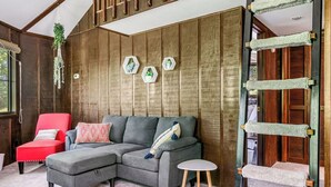 A modern living room with a sectional sofa, a red armchair, a small round table, and a wooden ladder.