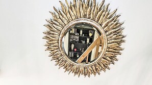 Escadaria em espiral com corrimãos de madeira e espelho com design de sol acima.