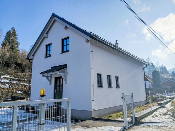 A white building with a sloped roof, a door, and three windows.