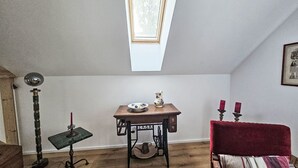 Um quarto com claraboia, uma mesa de máquina de costura, um abajur e uma cadeira vermelha.