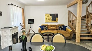 Uma sala de estar com lareira, sofá, mesa de jantar e cadeiras, e uma escada.