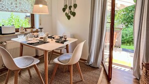 A dining area with a table set for two, a hanging plant, and a view of the outdoors.