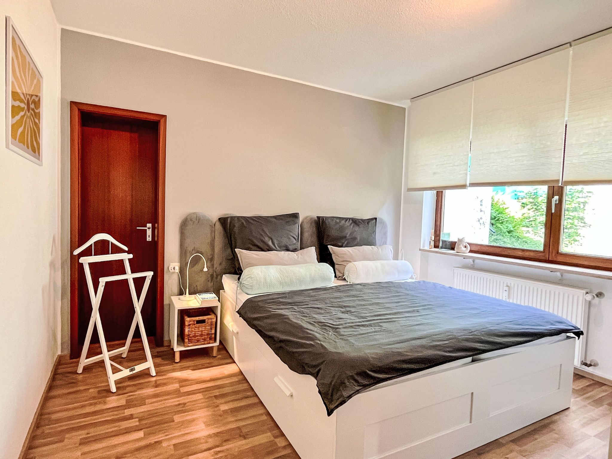 A bedroom with a bed, bedside table, lamp, and a window with blinds.