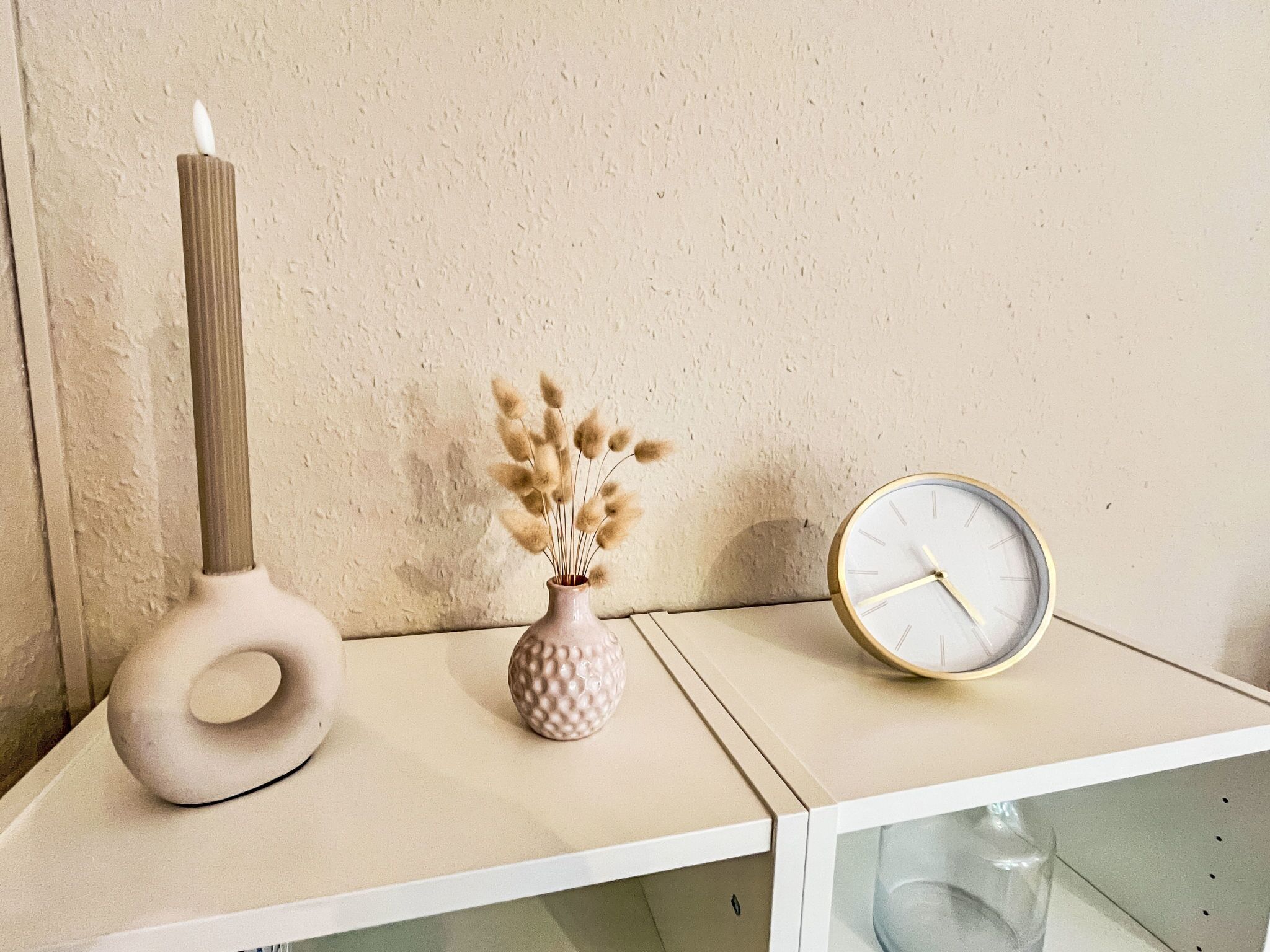 Une étagère avec une grande bougie, un vase rempli de fleurs séchées et une horloge ronde.