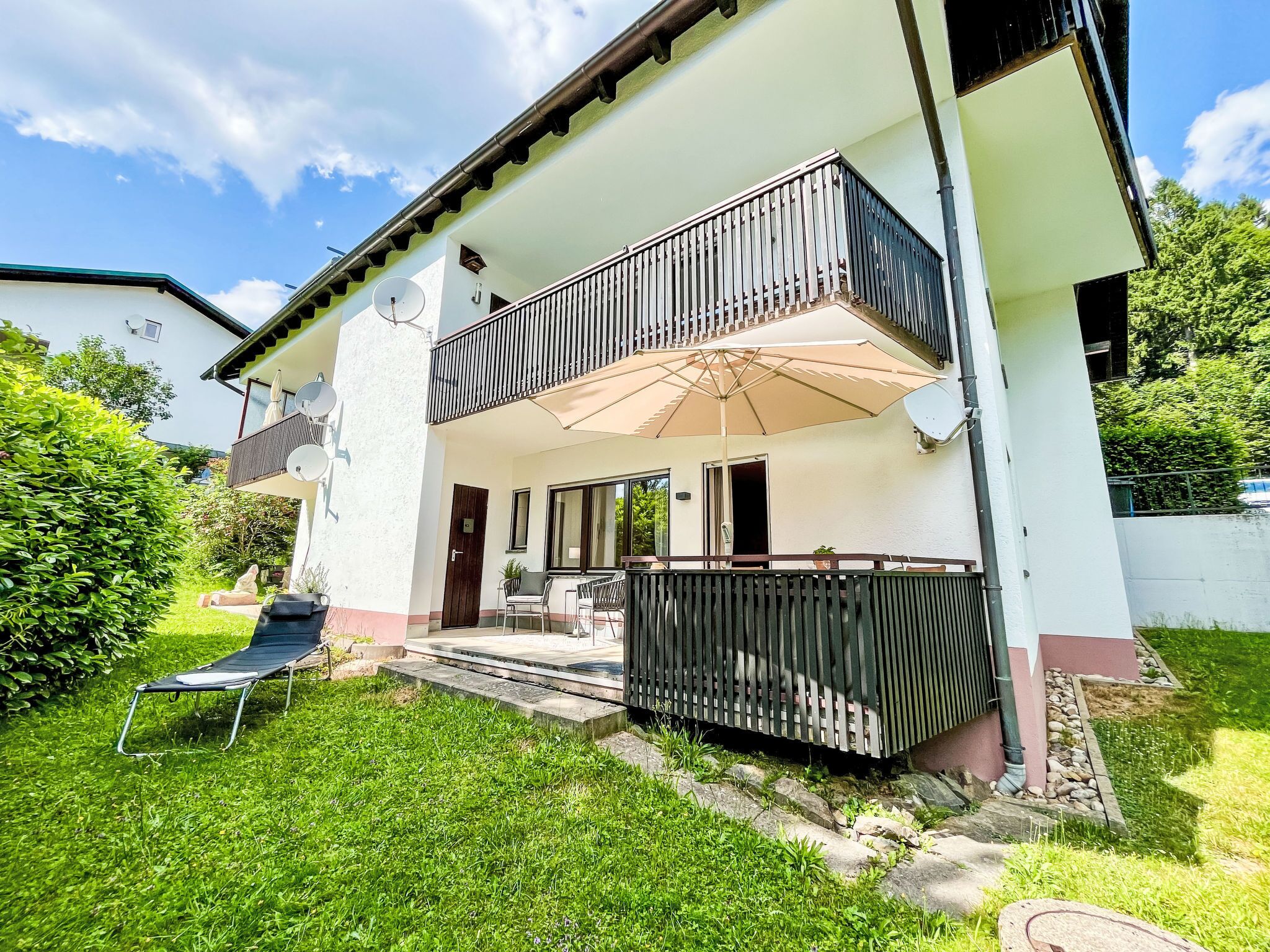 Ein zweistöckiges Haus mit Balkon, überdachter Terrasse und Rasen.