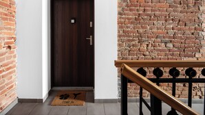 A wooden door with a digital lock, a doormat with a bird design, and a brick wall.