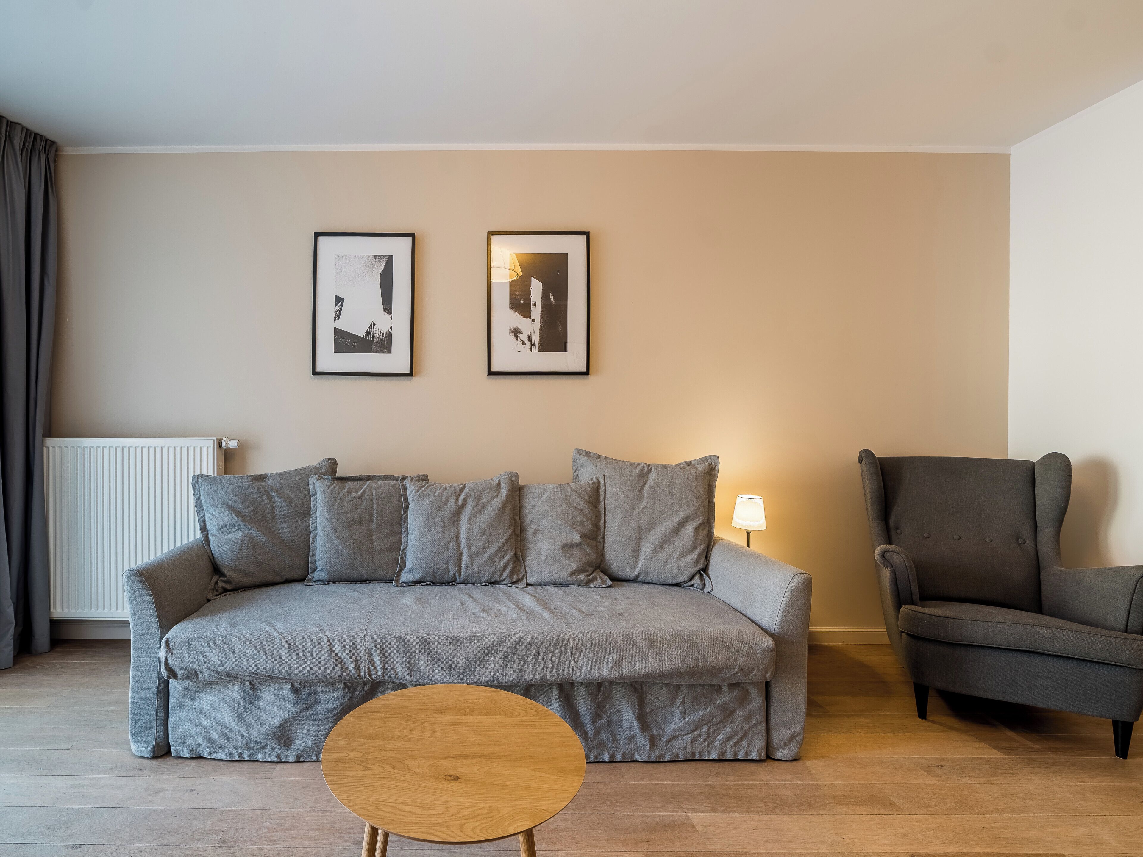 A modern living room with a grey sofa, a round wooden coffee table, a grey armchair, and two framed pictures on the wall.