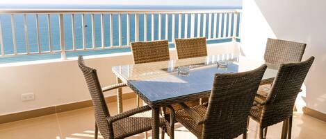Un balcón con una mesa de vidrio y sillas de mimbre, con vistas al mar.