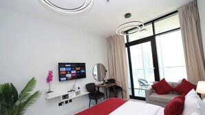 Une chambre d’hôtel moderne dotée d’un grand lit, d’un bureau avec une chaise, d’un téléviseur fixé au mur et d’un balcon offrant une vue sur la ville.