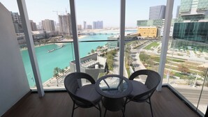 Un balcon agrémenté de fauteuils en osier et d’une table en verre, offrant une vue sur un paysage urbain avec une rivière et des bâtiments modernes.