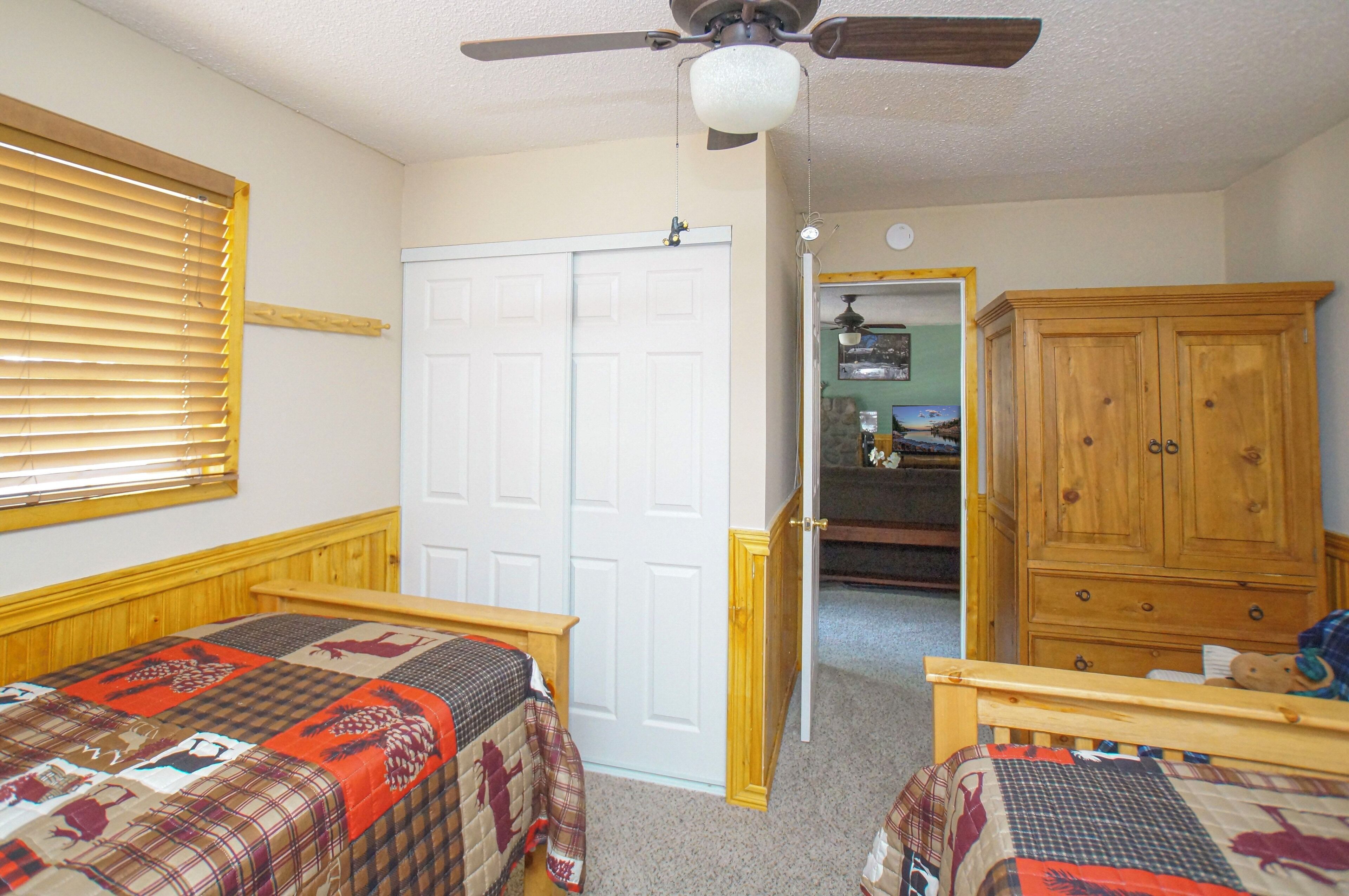 A bedroom with two beds, a wardrobe, and a ceiling fan.