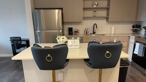 Une cuisine moderne dotée d’un îlot central, d’appareils électroménagers en acier inoxydable et de tabourets de bar.