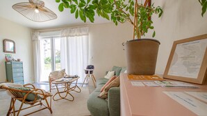 Een gezellige woonkamer met een groene bank, rieten stoelen, een kleine tafel en een grote potplant.