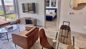 Uma sala de estar moderna com um sofá, poltronas, uma mesa de centro de vidro e uma TV na parede.