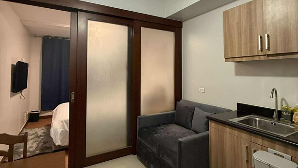 A compact living space with a kitchenette, a sofa, a ceiling fan, and a sliding door leading to another room. -  1- BEDROOM MARTEL 603 VERDON PARC (Davao City)