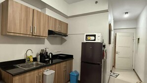 A compact kitchen with wooden cabinets, a black countertop, a stainless steel sink, a microwave, and a black refrigerator. -  1- BEDROOM MARTEL 603 VERDON PARC (Davao City)