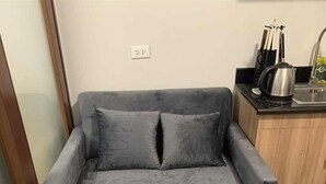 A grey sofa with two cushions in a room with a wooden cabinet and a kettle on the counter. -  1- BEDROOM MARTEL 603 VERDON PARC (Davao City)