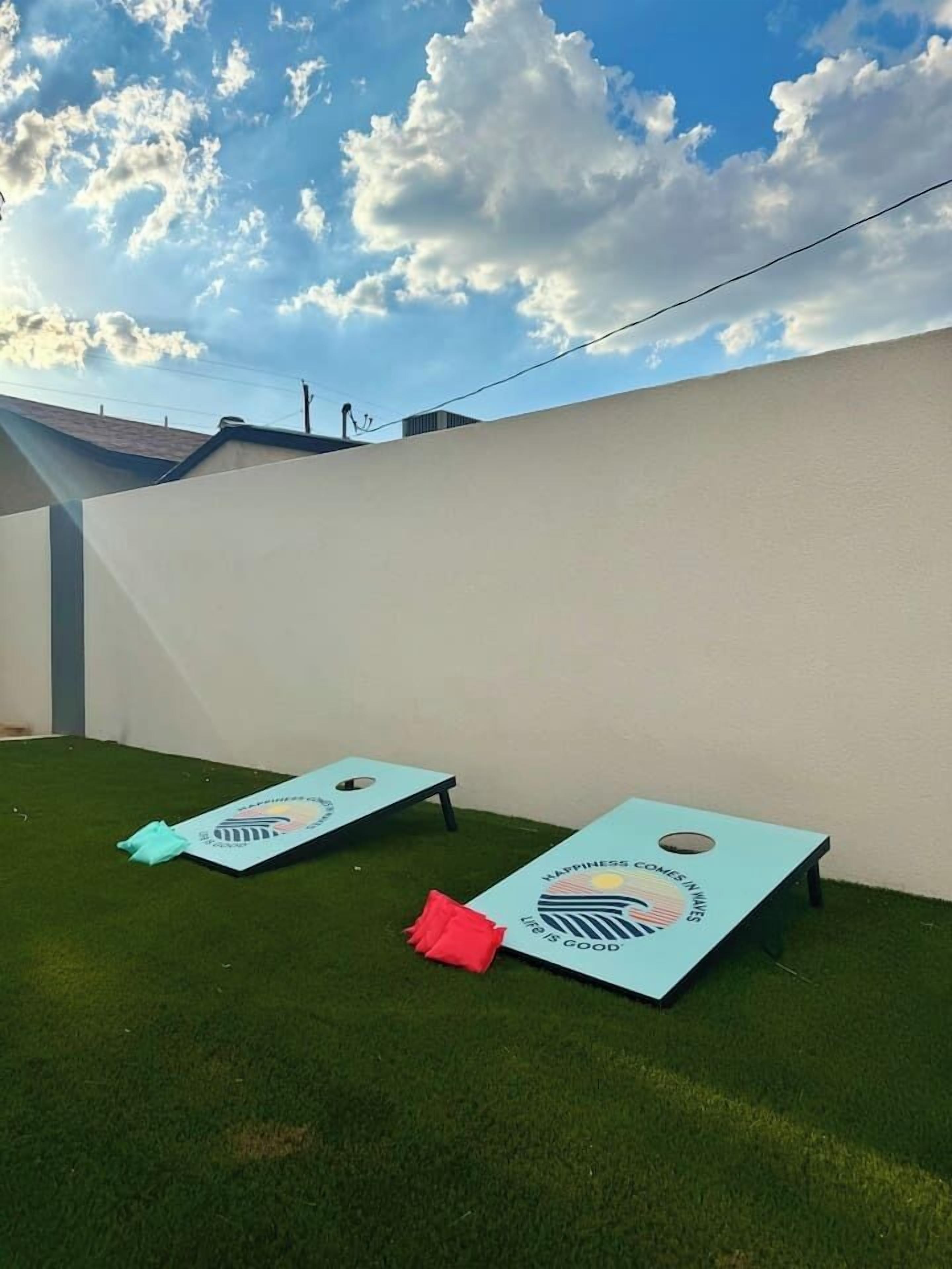 Two blue lawn games on a grassy area with a white wall and a clear sky.