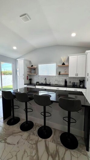 Una cocina moderna con armarios blancos, encimera negra y una isla central con taburetes de bar.
