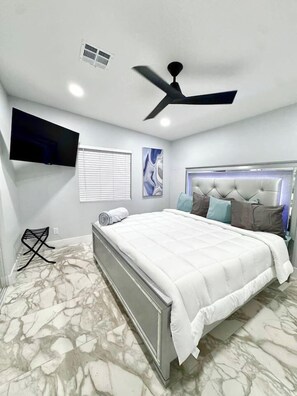 A bedroom with a bed, ceiling fan, TV, and marble-patterned floor.