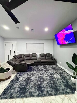 A modern living room with a sectional sofa, a mounted TV, and a marble floor.