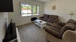 Un salon comprenant un canapé, une table basse, un téléviseur et une fenêtre donnant sur des immeubles.